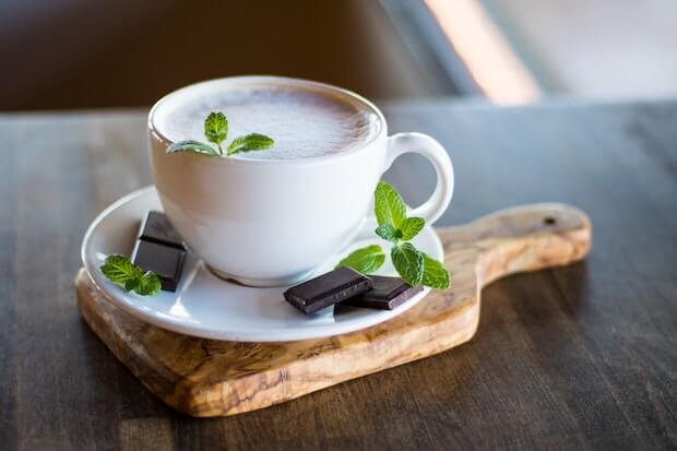 taza de capuccino decorada con hojas de menta y chocolate